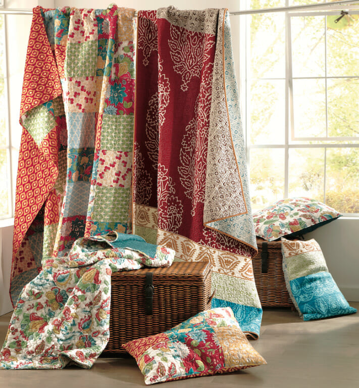 Colorful quilts draped over a rod and wicker basket, with matching pillow shams tossed nearby.