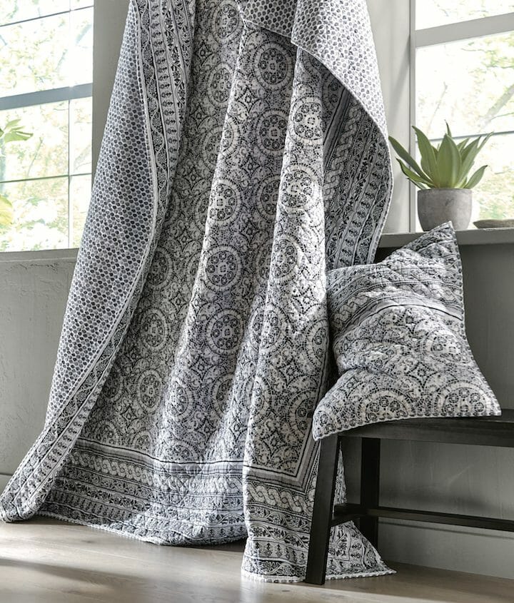 A black and white baroque quilt with a matching pillow sham displayed by gray paned windows.
