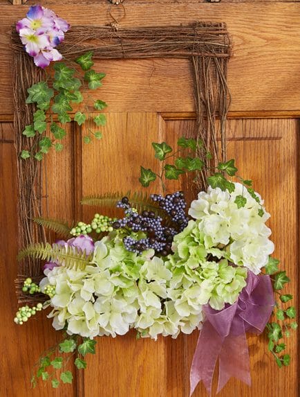 square twig wreath adorned with purple berries, green ivy, and hydrangeas, hanging on a wood door