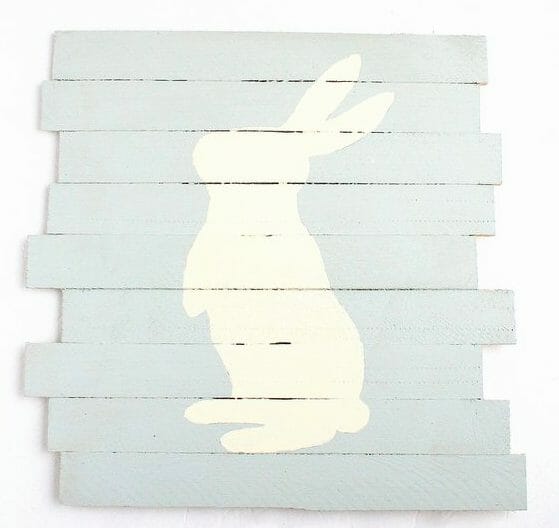 Stacked wooden pallet boards painted a pastel green is the background for a white painted bunny