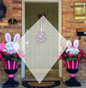 A front door hung with a wreath, and Easter Bunny decor in matching urns, with a screened triangle overlay.