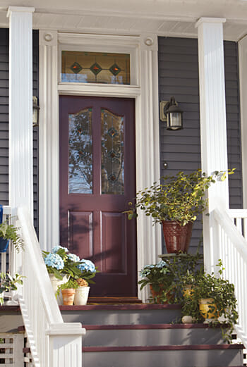 A Victorian home's front porch with stained glass, and potted plants on the steps, with potted blue hydrangeas.