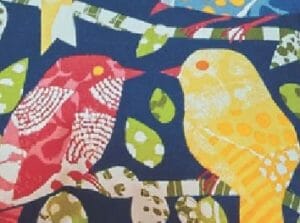 A fabric swatch in a multicolor pattern of quilt-like birds on branches with leaves.