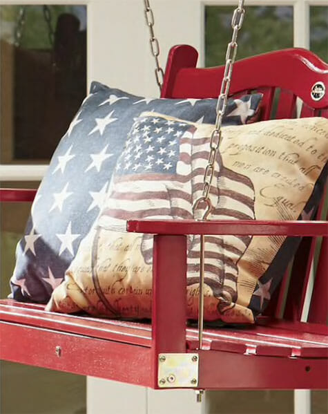 Americana flag and star pillows on a red front porch swing.