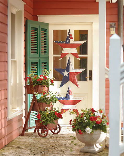 A side front door with Patriotic stars, a green shutter, a stepped planter and an urn of red and white geraniums.