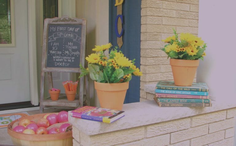 a bushel of apples, stacks of books, and a chalkboard easel create a back to school themed front porch