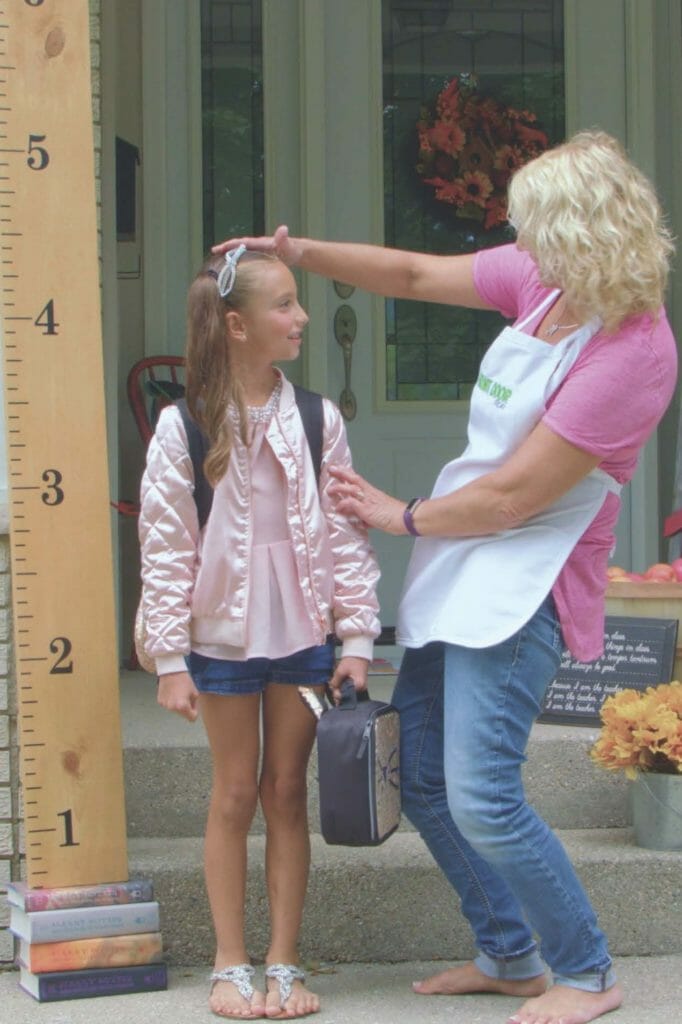 woman measuring girl with large vertical wood ruler on front porch for a back to school themed porch