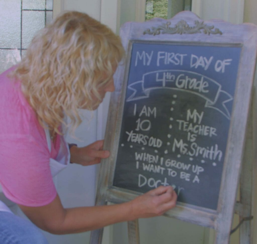 woman writing on chalkboard with my first day of school info for a back to school themed front porch
