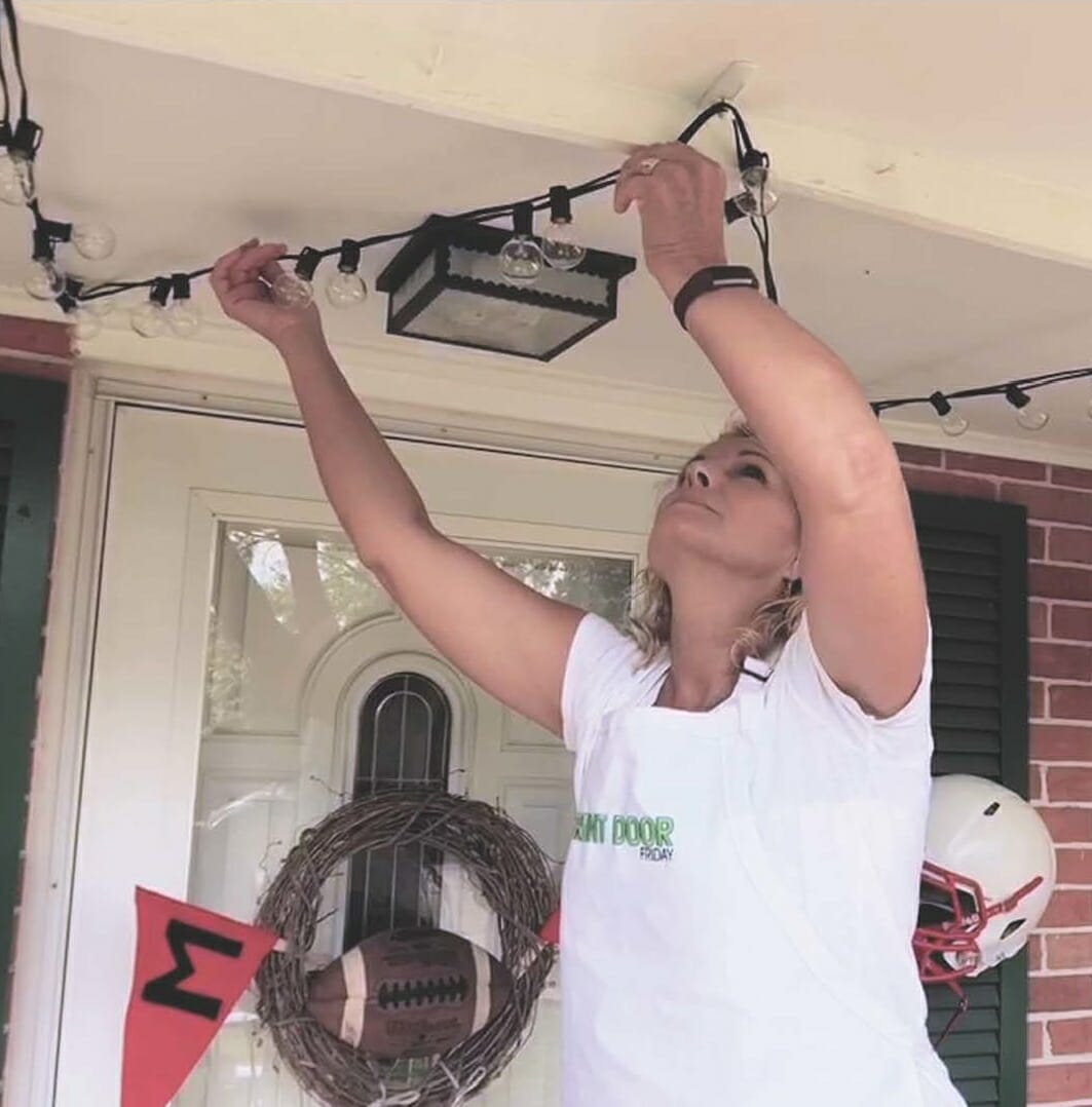 woman hanging lights on front porch ceiling for football themed porch