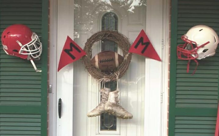 football themed wreath hanging on front door, made from football cleats, football helmets, and flags