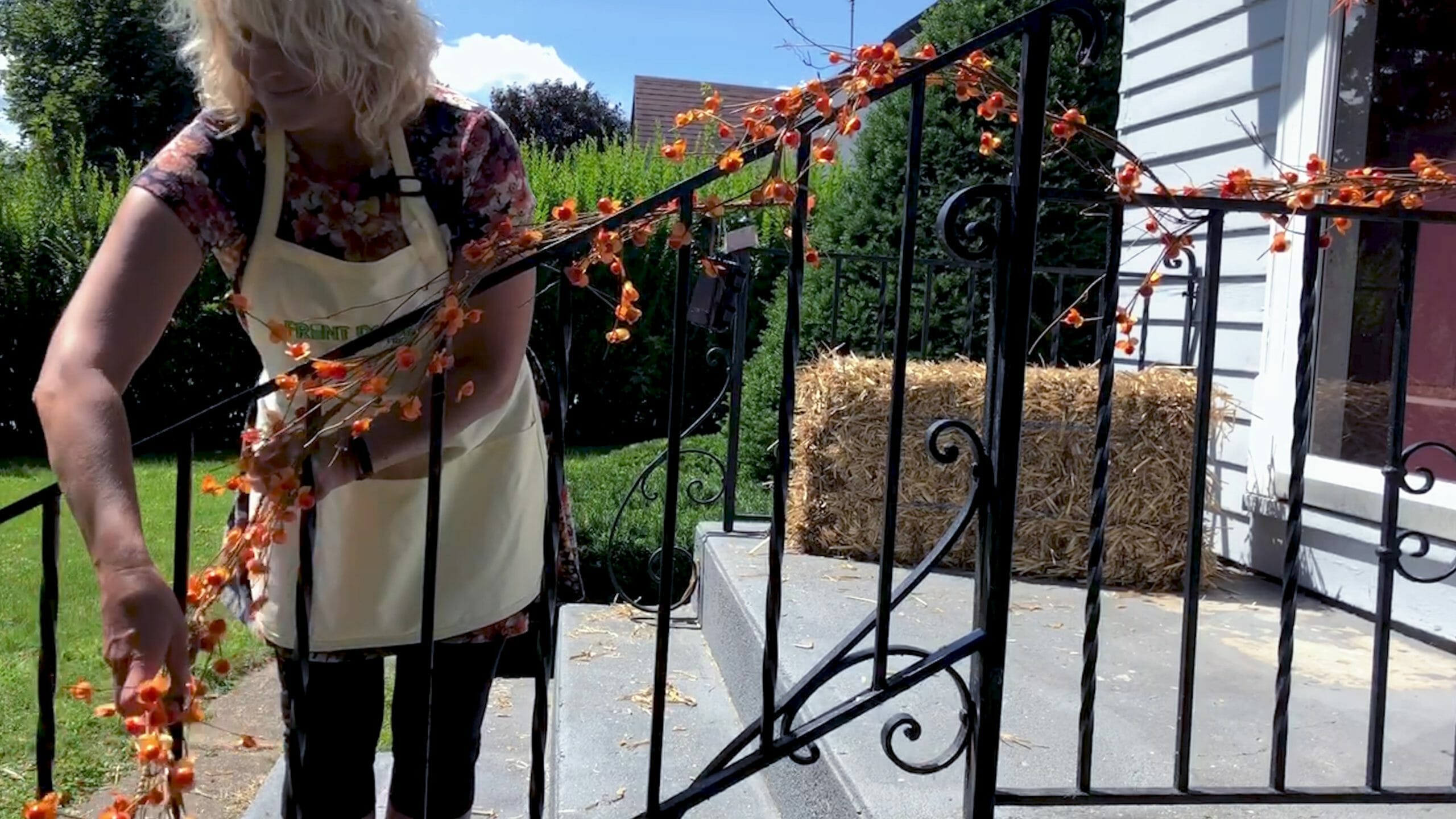 woman weaving bittersweet garland around a wrought iron railing on steps for a fall themed porch