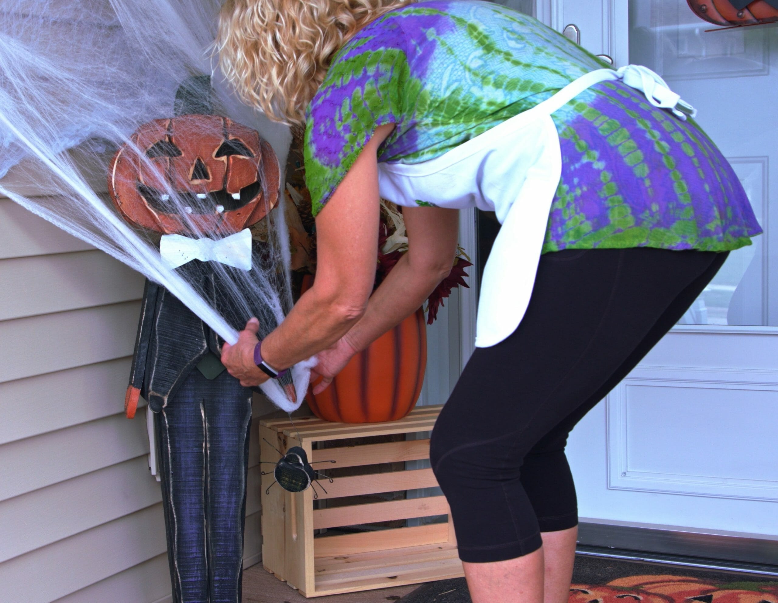 woman hanging cobwebs on wooden pumpkin person