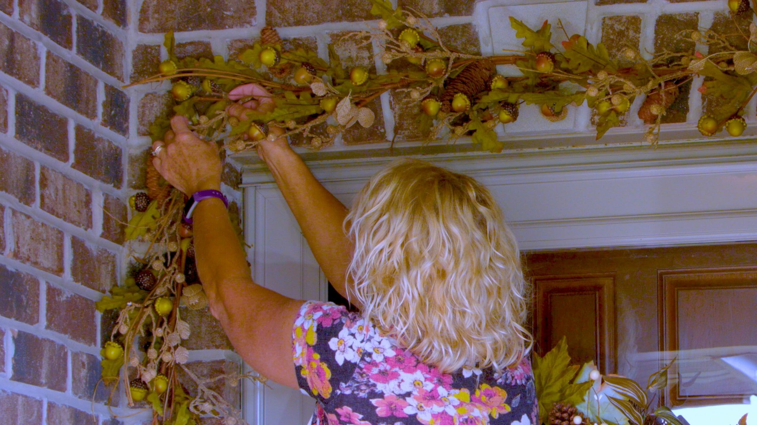 woman hanging garland over door that consists of branches of acorns pinecones and leaves