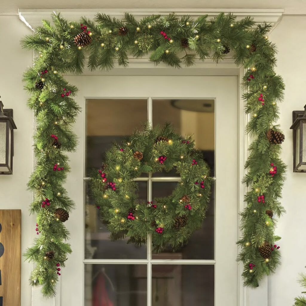 front door garland and wreath adorned with evergreens lights pinecones and poinsettia
