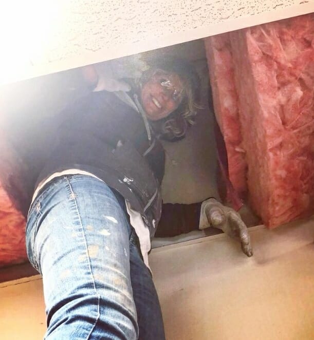 woman waving while looking down from an attic full of insulation