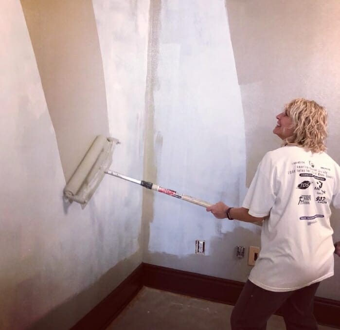 woman using a large paint roller to paint a wall beige