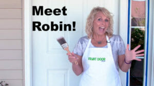 Meet Robin! – A laughing blonde woman in a white Front Door apron, standing by a white door with a paintbrush in her hand.