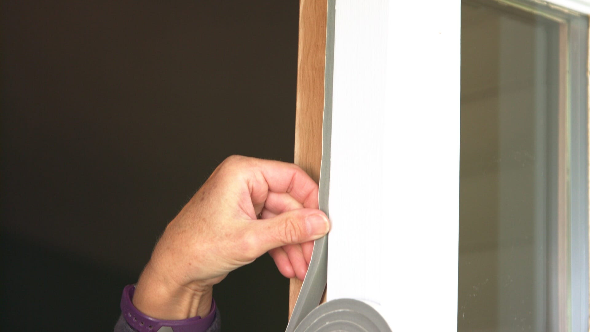 woman applying weather stripping to side of door frame