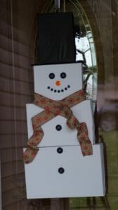 A DIY snowman with a black hat and a ribbon scarf on a front door.