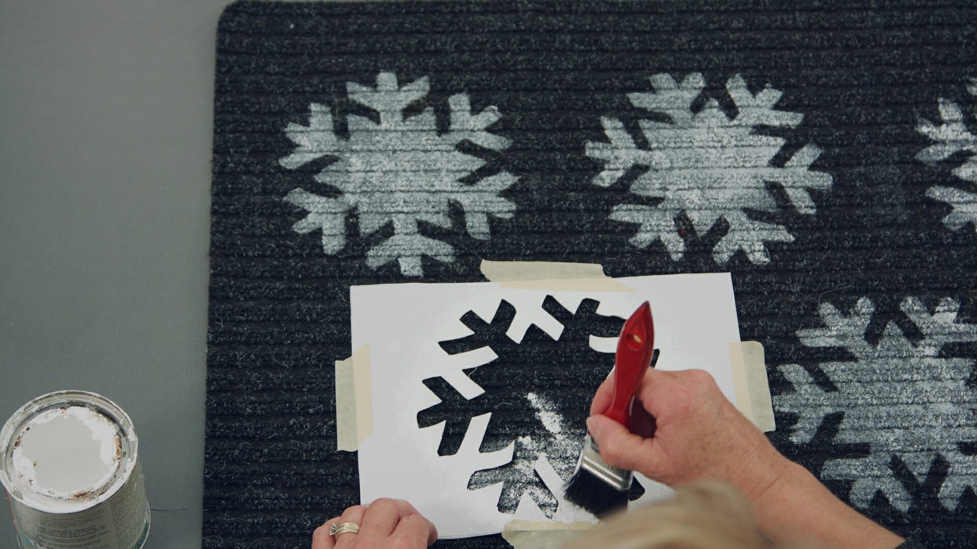 woman painting white snowflakes on black matt using stencils