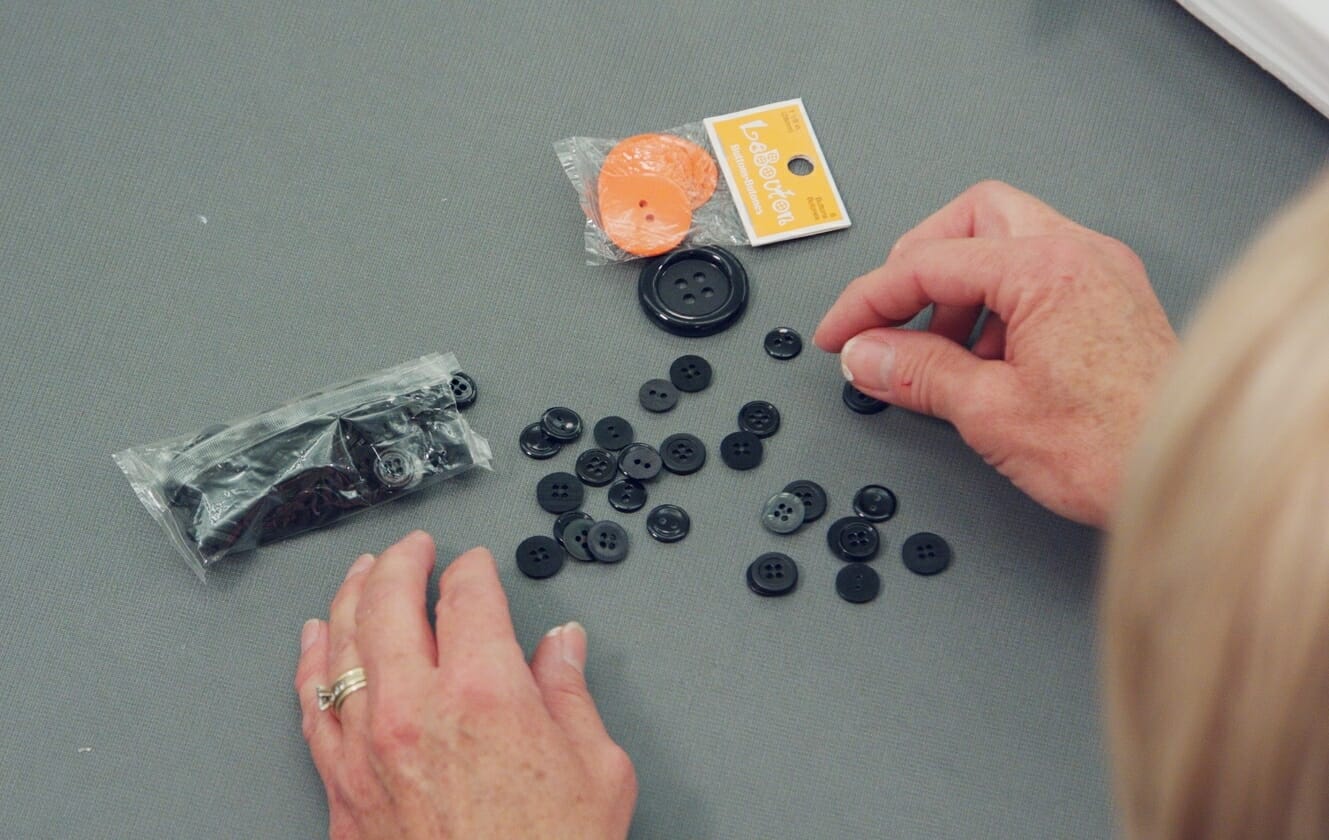 woman sorting through various sizes of black buttons