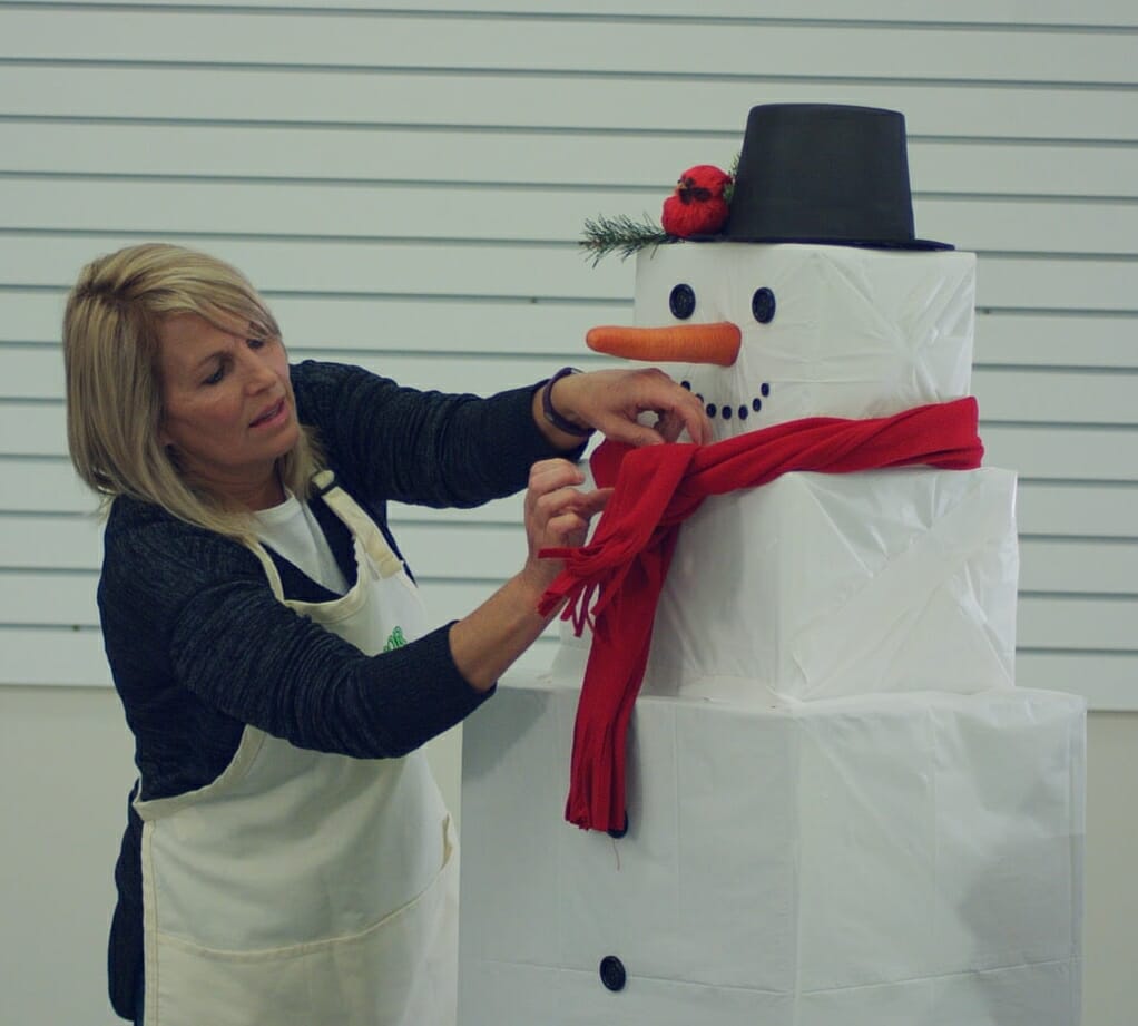 woman tying red scarf around Snowman's neck