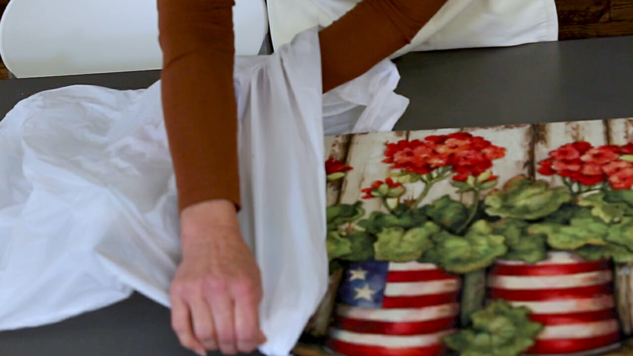 A woman placing a Patriotic red geranium doormat into a white plastic bag for storage.