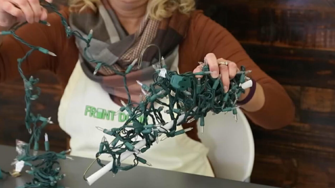 woman wrapping Christmas lights around a metal clothes hanger for storage