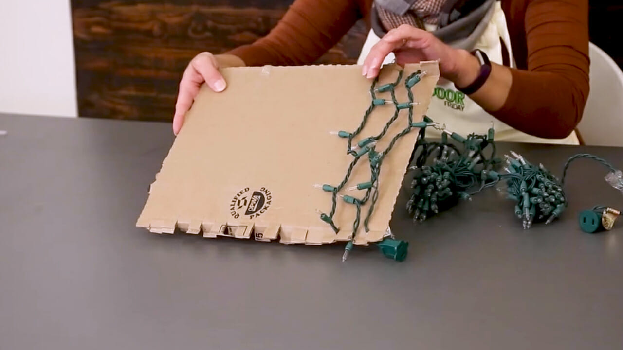 woman wrapping Christmas lights around a piece of cardboard for storage