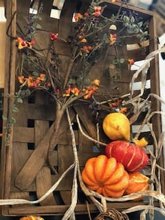 A square woven basket with bittersweet branches, rafia, and orange gourds.