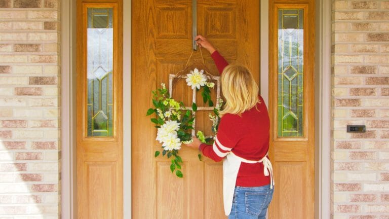 woman hanging a wreath on front door made from a window frame and white and green flowers