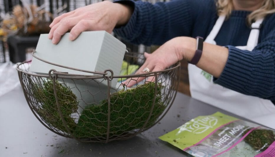 woman placing a foam block in metal wire flower basket