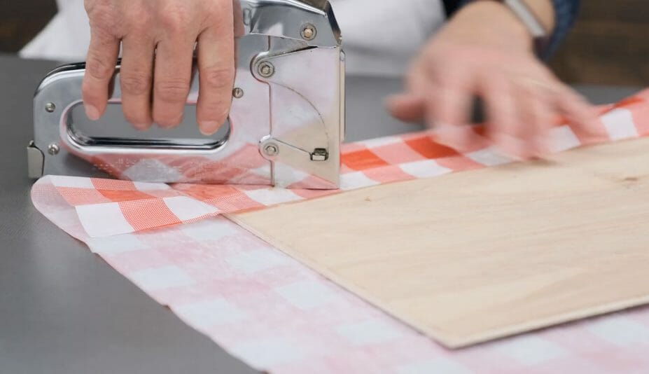 woman stapling red and white gingham material on board