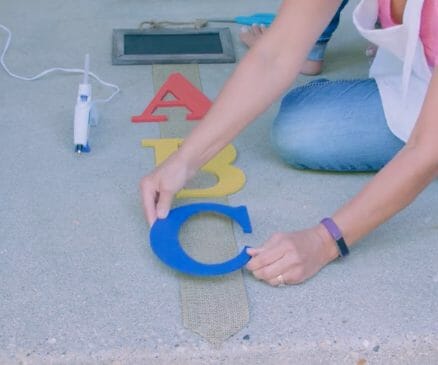 woman applying glue to the ABC letters to affix to burlap ribbon to create a back to school themed décor