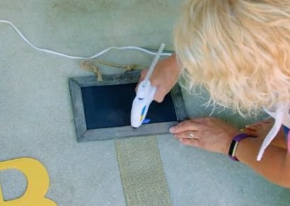 woman applying hot glue to back of chalkboard to affix letters and burlap for back to school themed décor