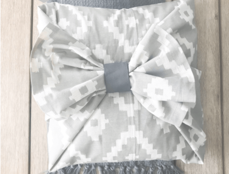 A grey and white print pillow with a large fabric bow.