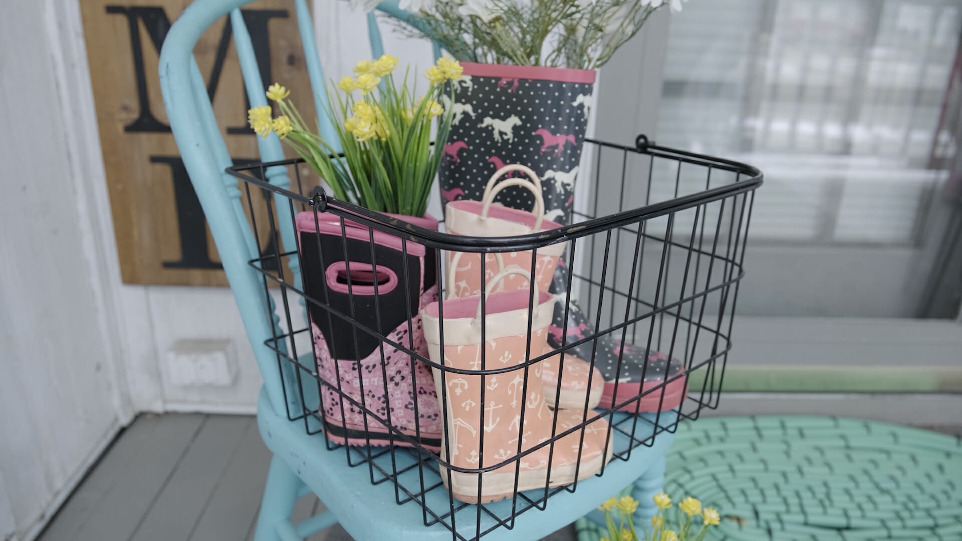 black basket on chair full of rubber rain boots with flowers for a spring themed front porch