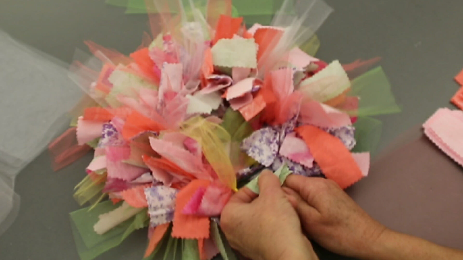 Close up view of a woman's hands assembling a colorful rag wreath.