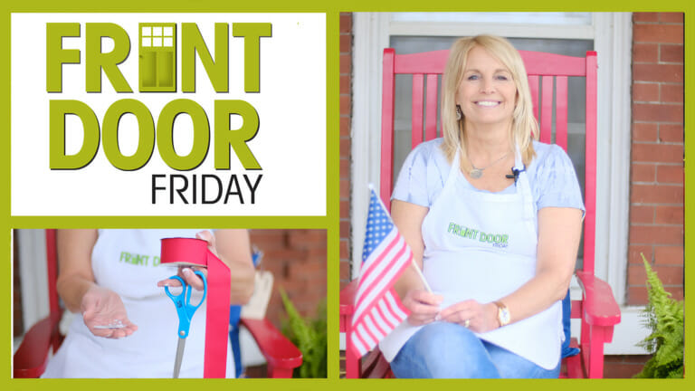 Front Door Friday – Smiling woman on a porch with a USA flag – Holding scissors and red ribbon for Americana decorating.