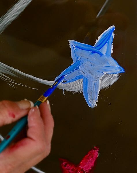 Close-up of a person painting a blue star on a glass door.