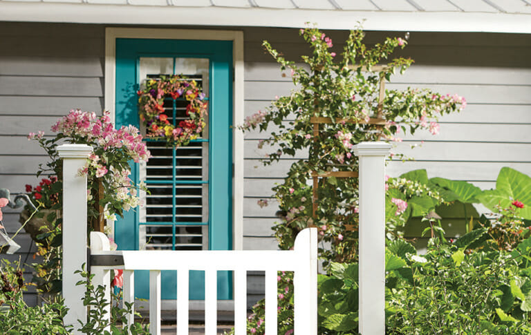teal door with a summer flowers wreath and a white picket fence