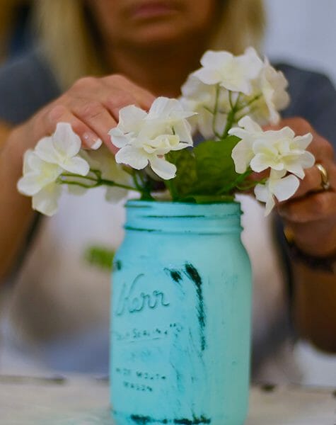 arranging flowers in painted teal Mason jar