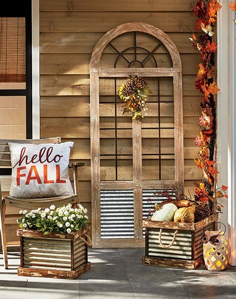 Hello Fall pillow on a wood chair, galvanized buckets with mums and gourds, a lit Fall garland and an owl lantern.