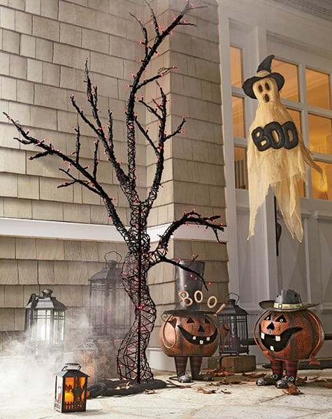 Hanging ghost by a front door saying Boo, a lit Halloween tree, metal bobble Jack-o-Lanterns, and lit lanterns.