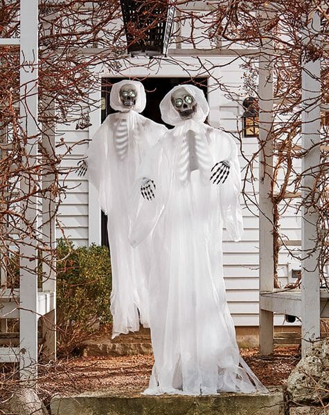 Two ghost skeletons hanging from an arbor covered in bare branches, in front of a black entrance door.