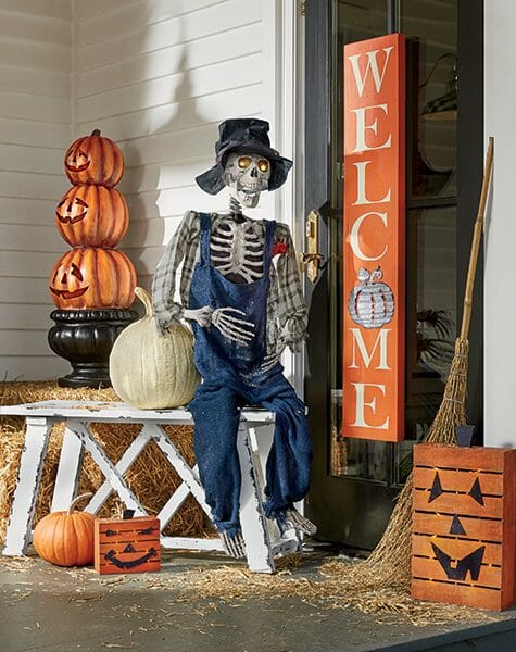 A hillbilly skeleton, pumpkins, a Jack-o-Lantern topiary, and a tall orange Welcome sign on the black front door.