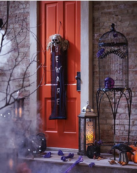 Creepy Halloween skeleton banner on an orange front door, a tall black birdcage, lit lanterns, crows, and smoke.