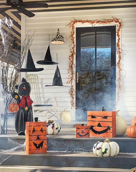 Hanging witch hats, wood Jack-o-Lantern and black cat cutouts, and bittersweet garlands over a black front door. 