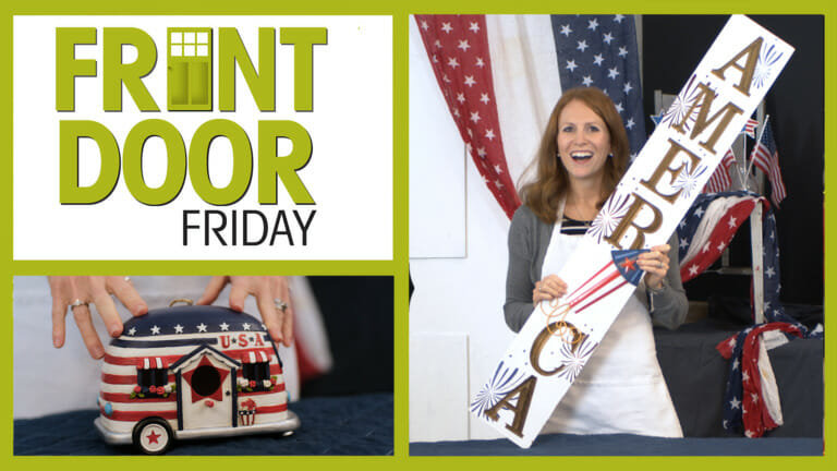 Front Door Friday – Smiling woman on a porch with Patriotic flags, swags, America plaque, and a USA travel trailer figurine.