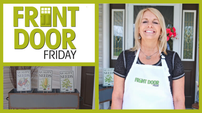 Front Door Friday – Smiling woman in an apron – Front porch with a metal planter with large seed packet signs.